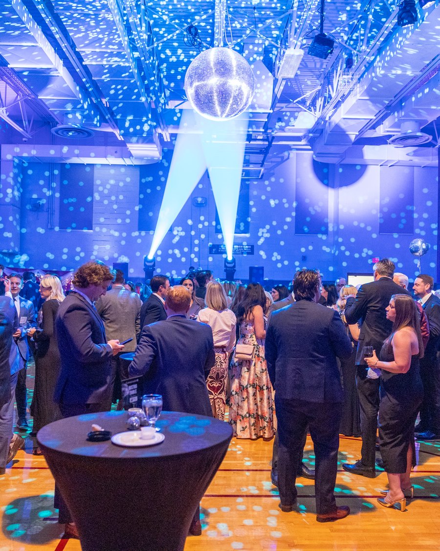 A packed event in full swing under a mirror ball and twin spotlight beams, the room washed in blue